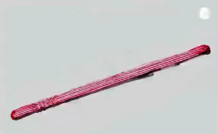 A long red-pink object with white streaks lies diagonally against a gray background, with a white circle at the upper right.