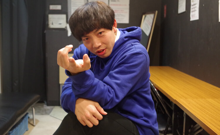 青いパーカー姿で片手を前に差し出すティモンディ前田。